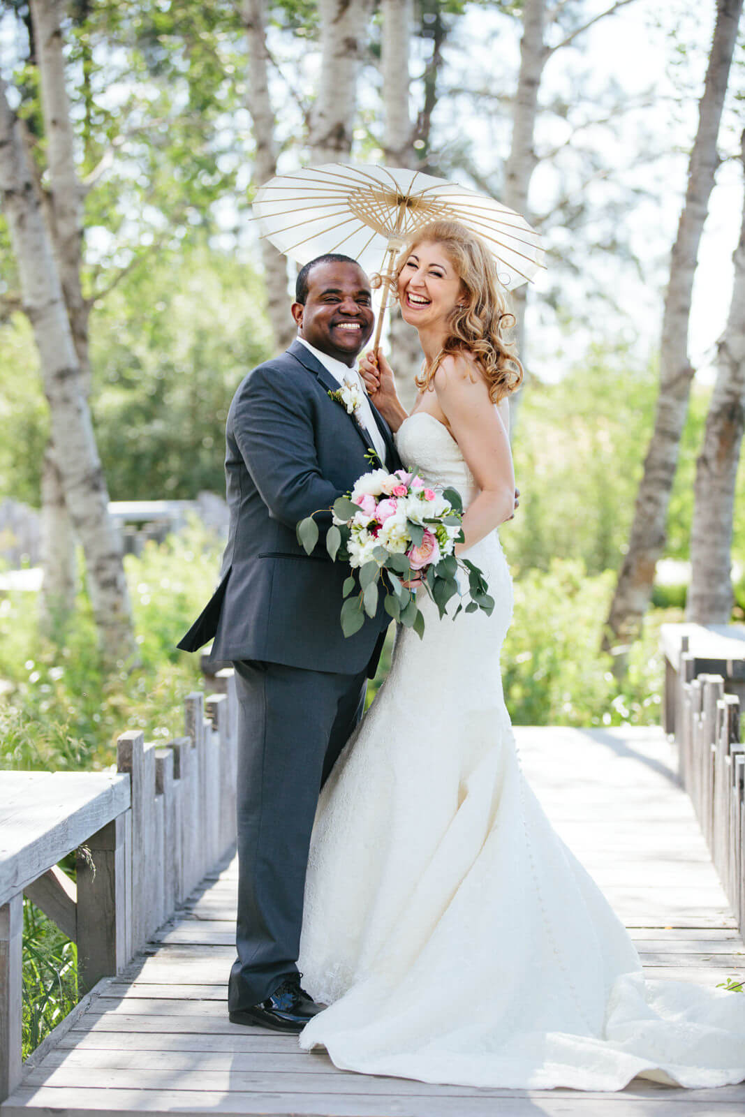 A bride and groom smile while holding a parasol at their wedding at Sky Ridge Ranch in Ronan Montana