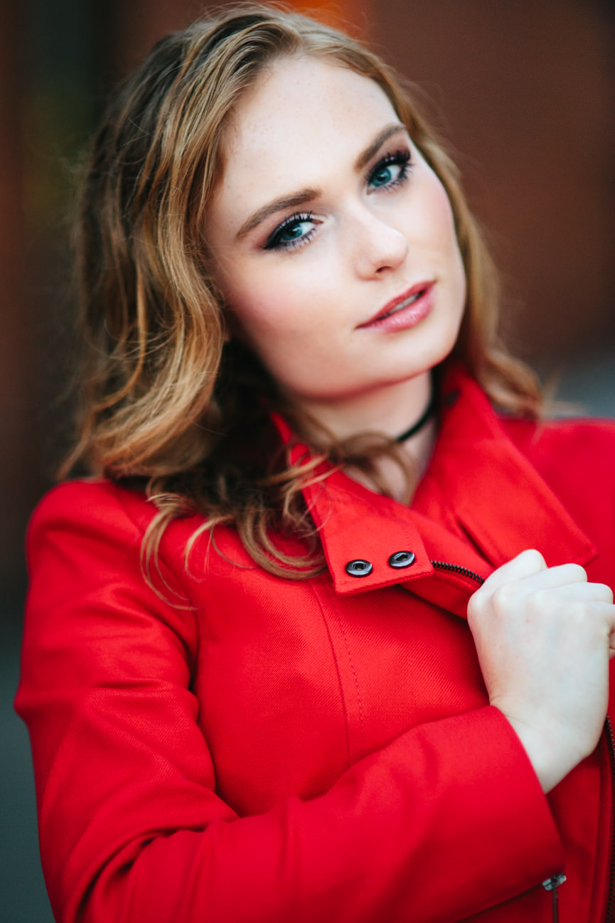 A young woman wearing a red jacket smiles for her headshots in Missoula Montana