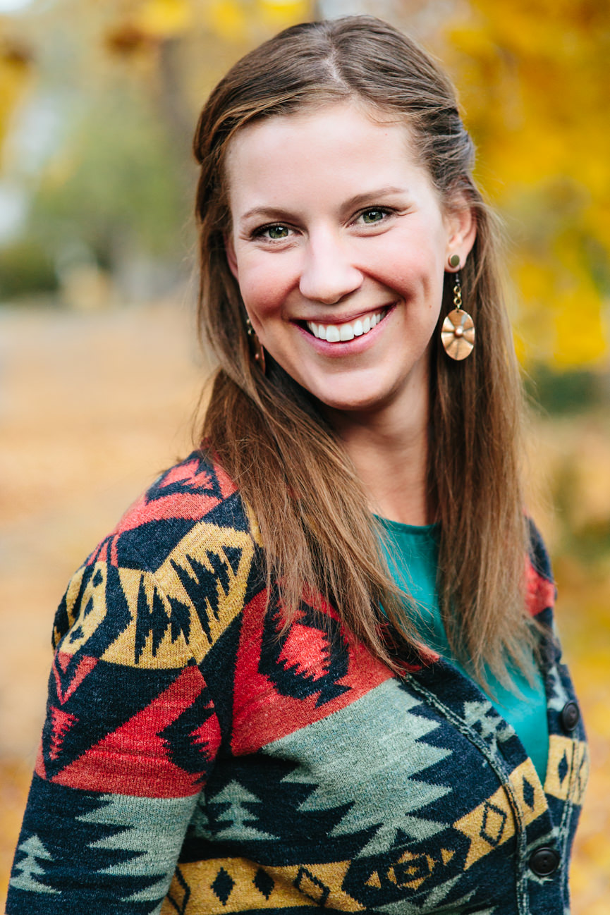 A woman wearing a multicolored jacket smiles for her headshots in Missoula Montana