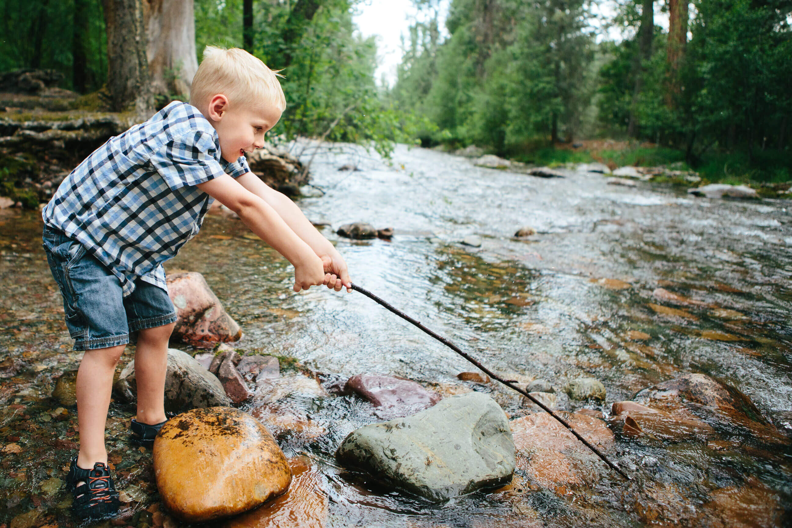 A young boy fishes with a stick in a creek in Missoula Montana
