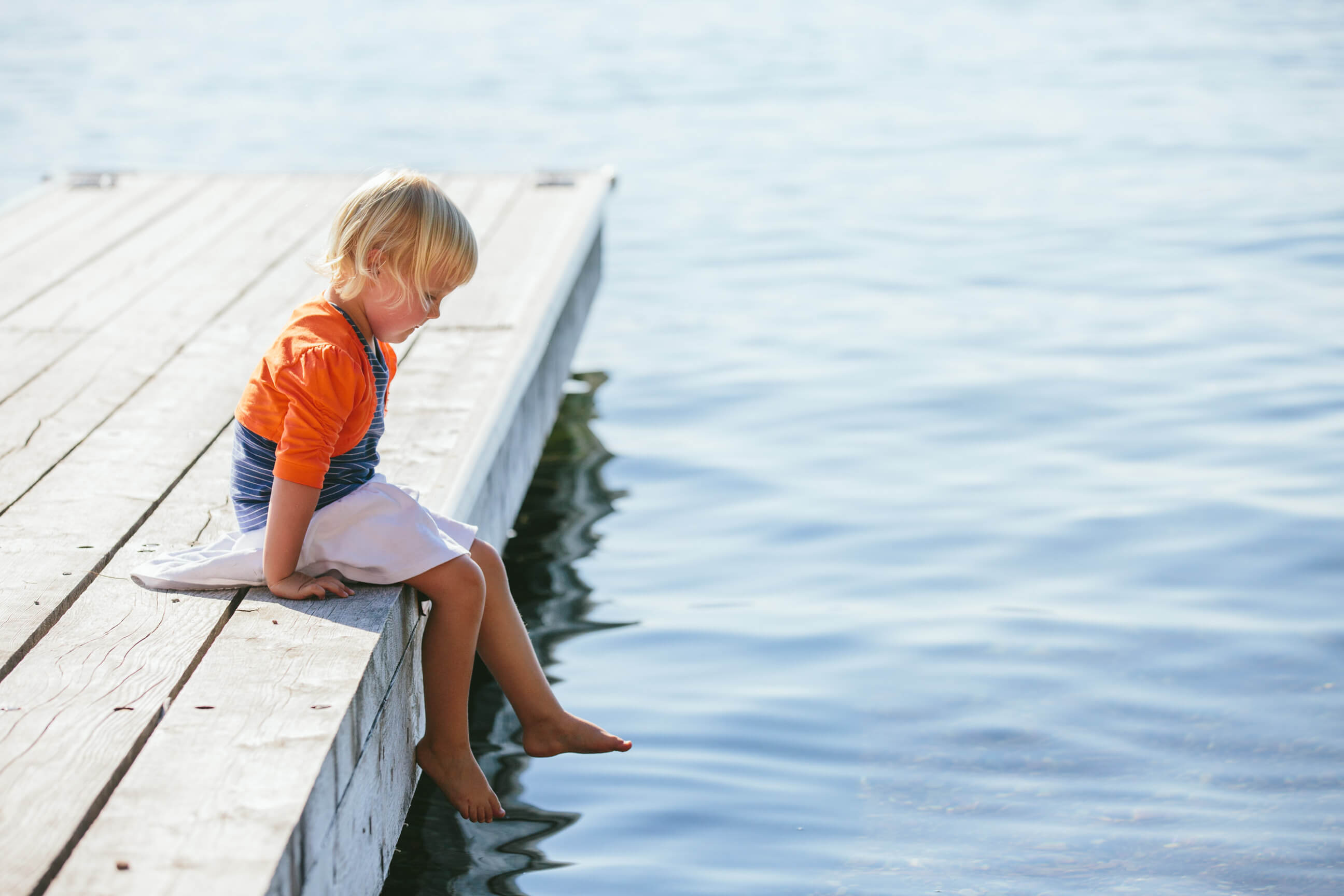 A young girl with bare feet sits on a dock on Flathead Lake in Montana