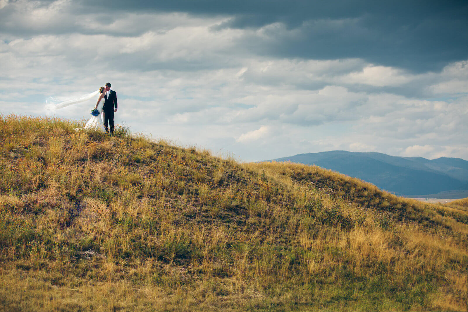 A bride's veil catches the wind as she kisses her groom at their wedding at the Barn on Mullan in Missoula Montana