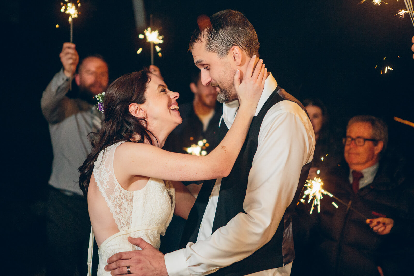 A bride and groom embrace as guests wave sparklers at their wedding at the Barn on Mullan in Missoula Montana