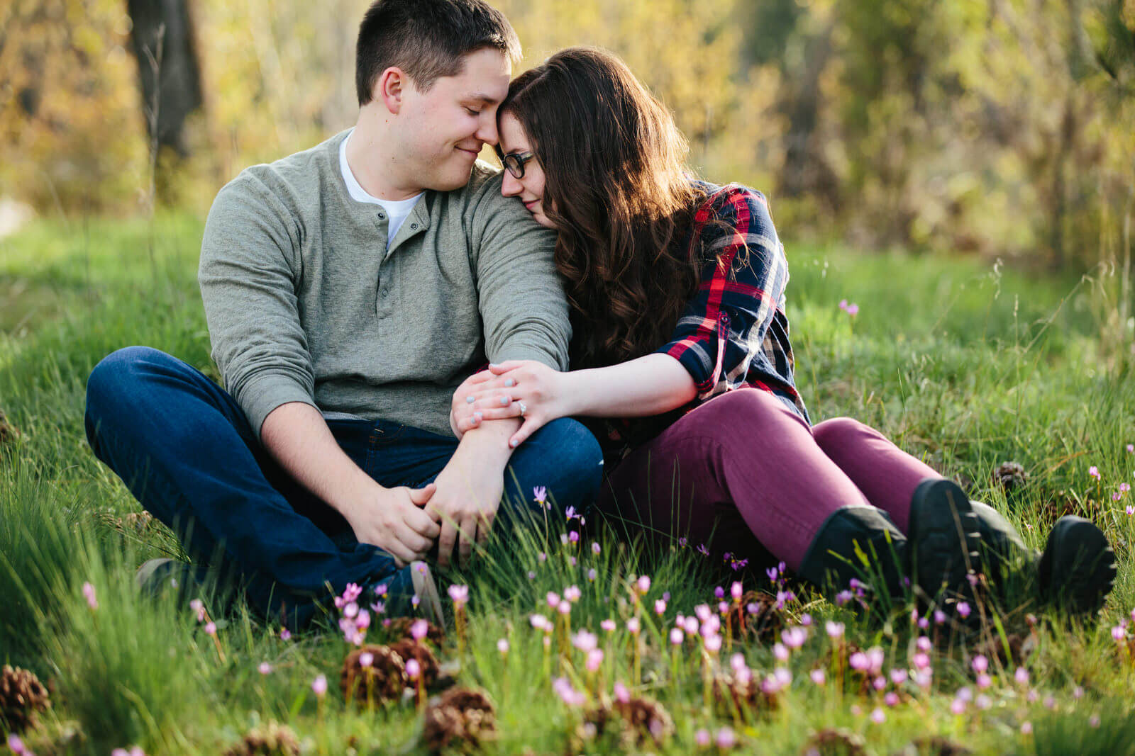 A couple places their heads together as they sit amongst shooting star wildflowers during their engagement session in Missoula Montana