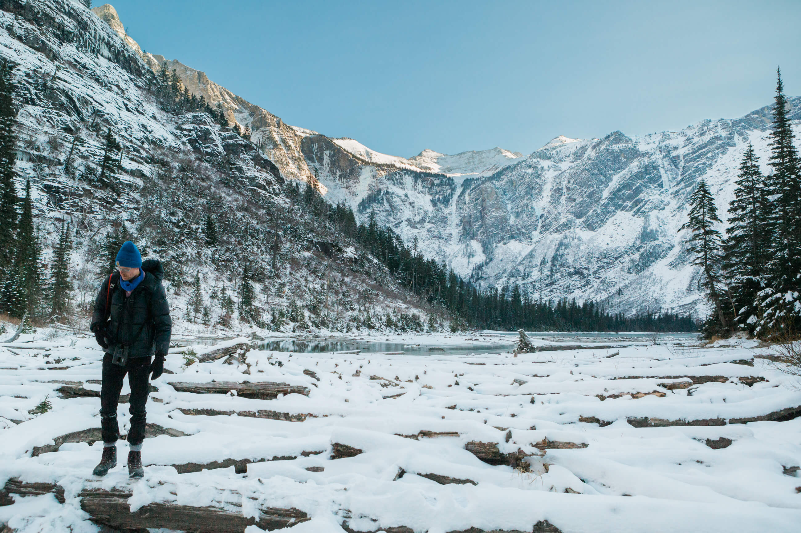 A man walks over snow covered logs near Avalanche Lake in Glacier National Park in Montana