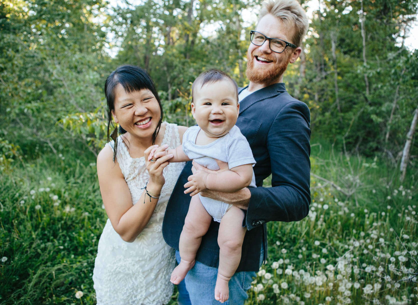 Parents and their baby laugh together and hold hands during their family portraits in Missoula Montana