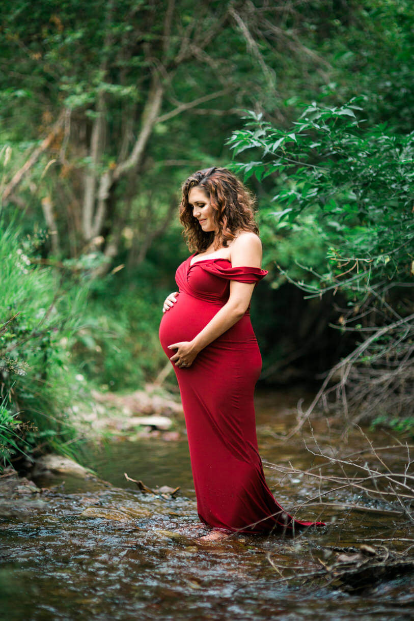 A pregnant mother stands in a creek and looks down at her belly during her maternity session in Missoula Montana