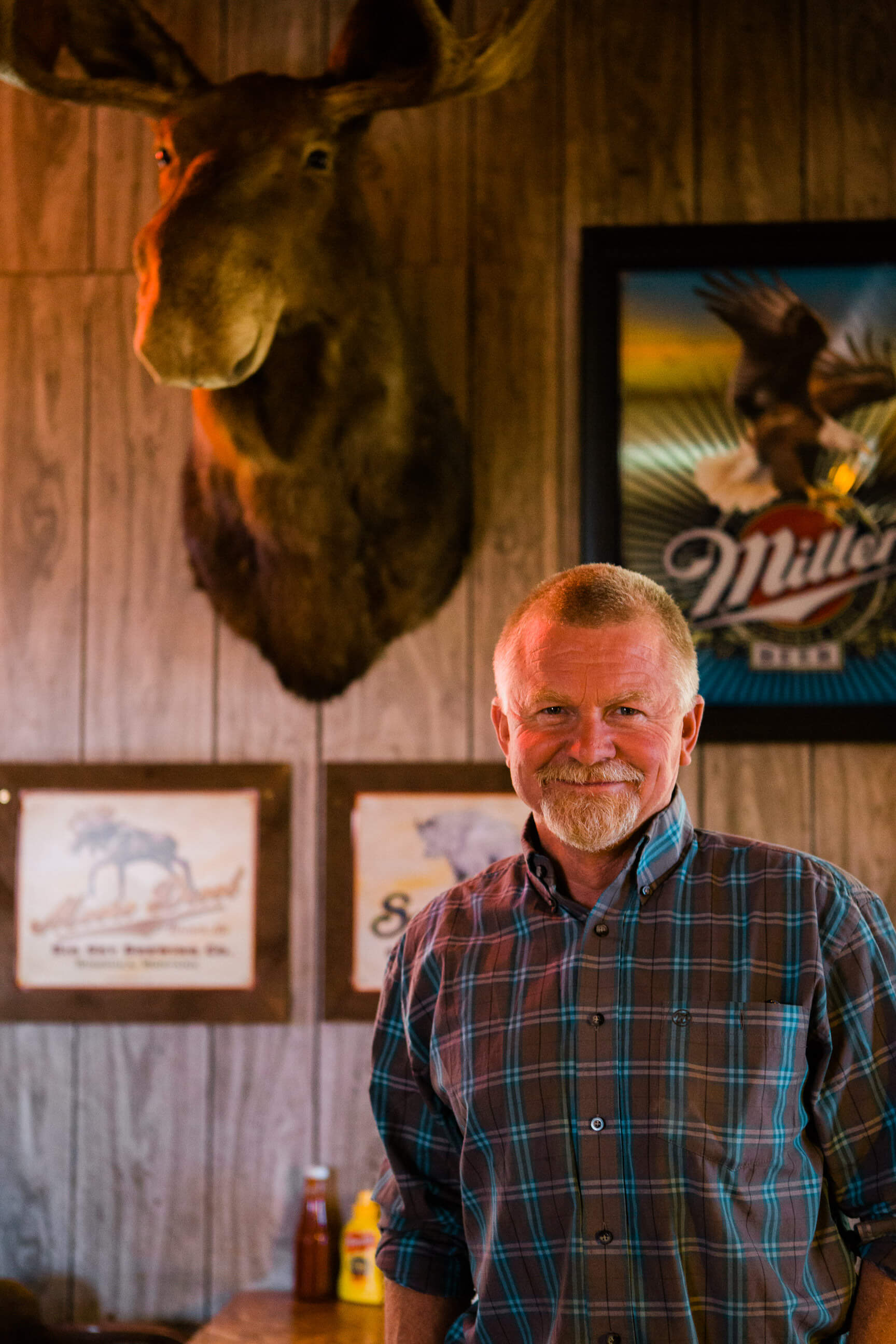 A man poses in front of a mounted moose head at a bar in Ovando Montana
