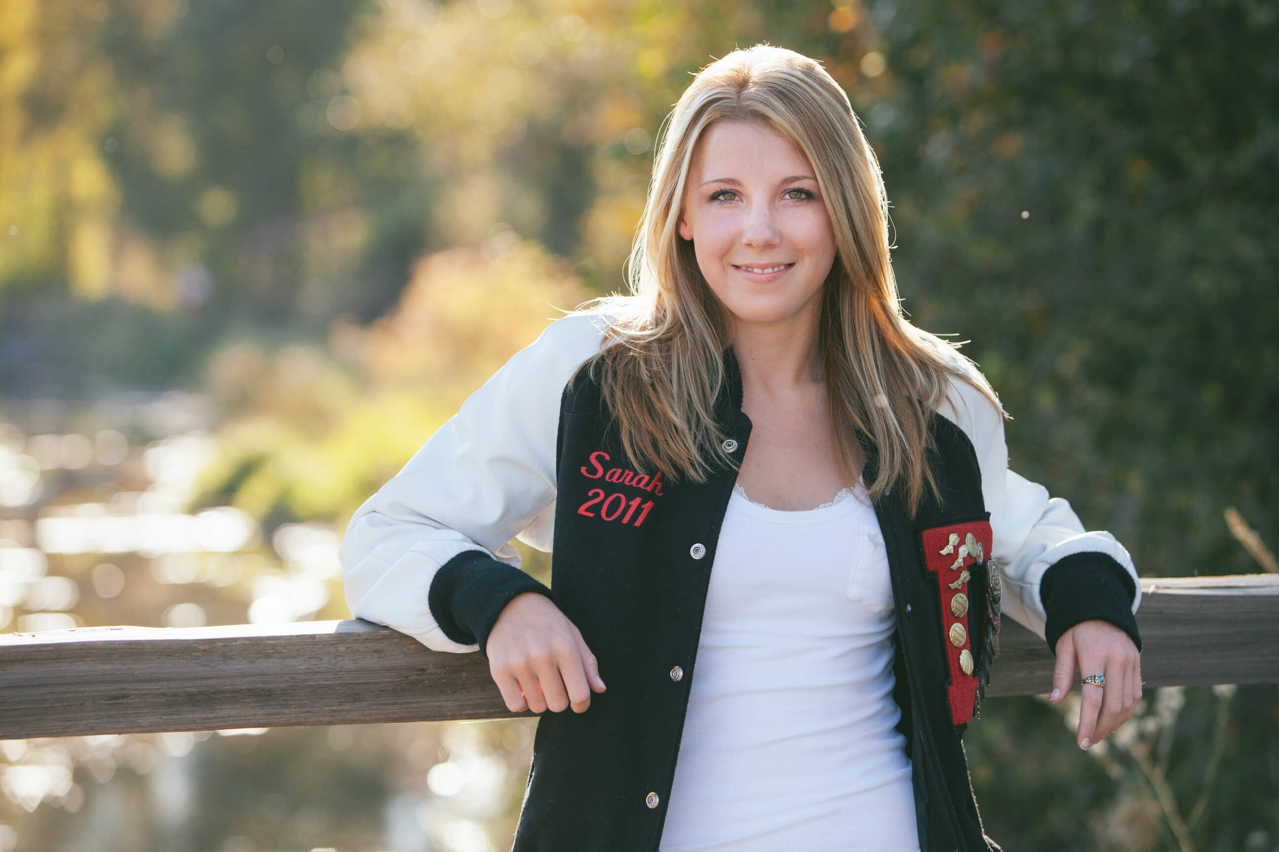 A senior girl smiles and leans on a fence at her senior photo session in Stevensville Montana