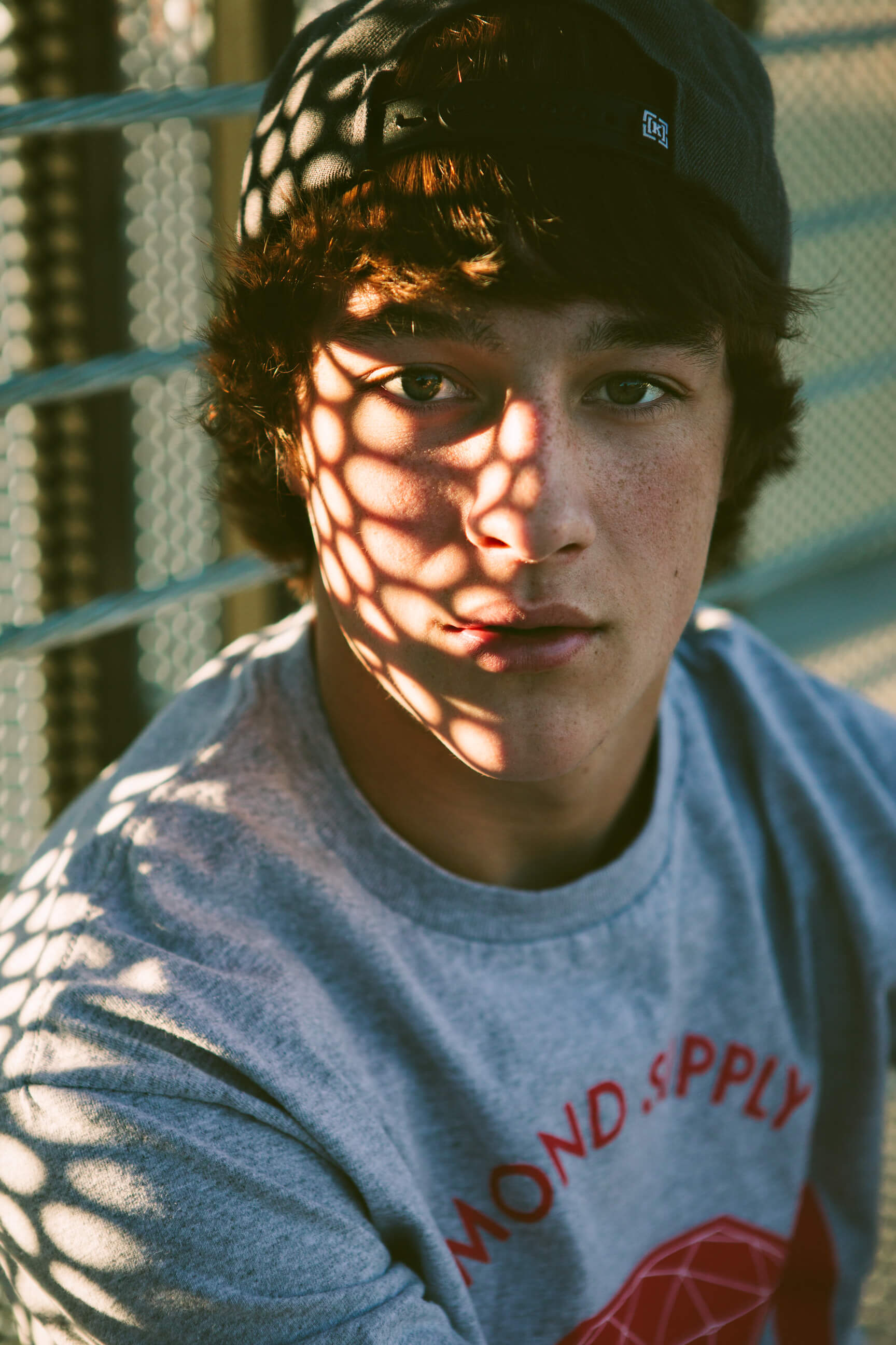 A senior boy in dappled light looks at the camera during his Missoula Montana senior portrait session