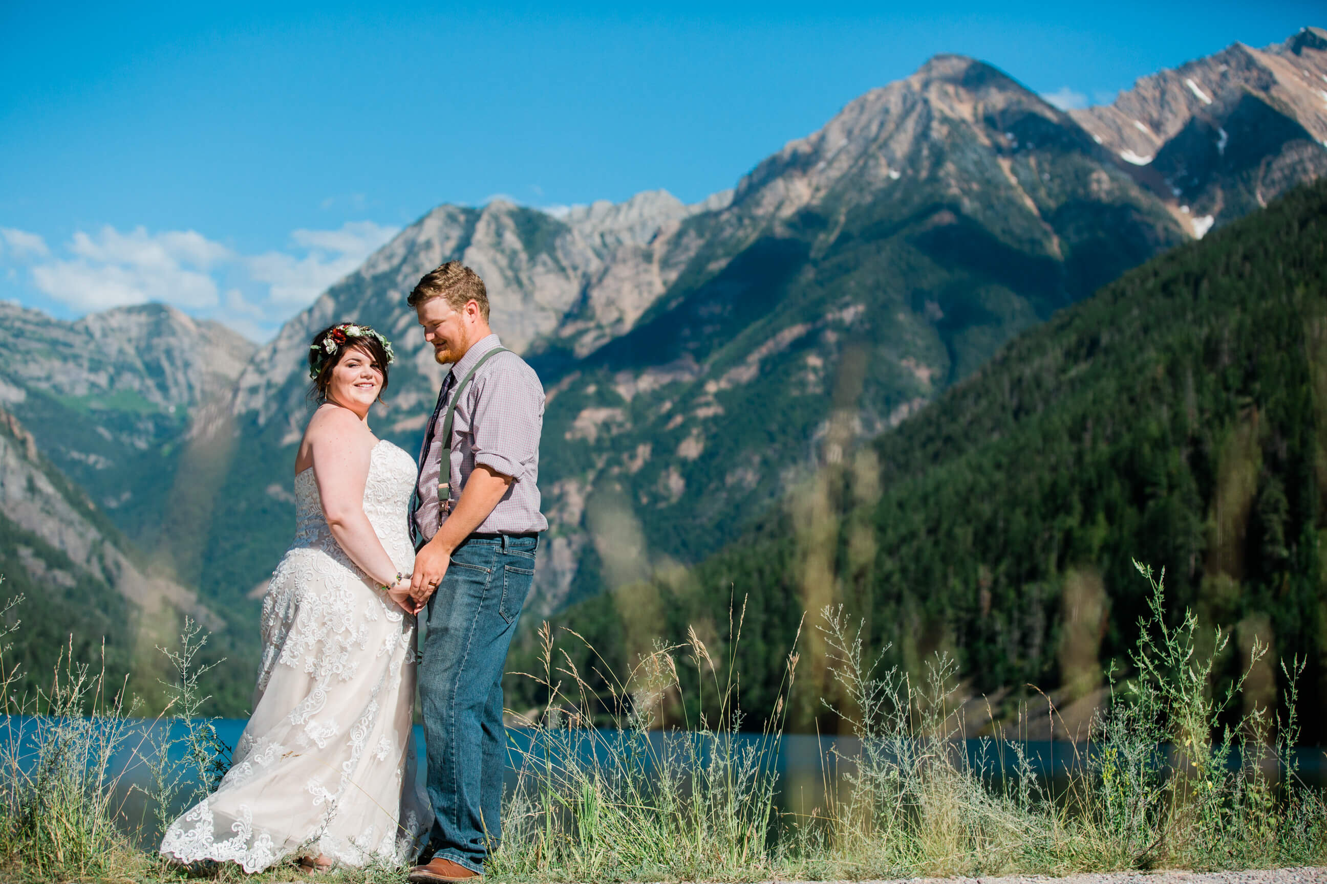 A bride and groom smile as they stand in front of mountains and a lake during their Montana elopement