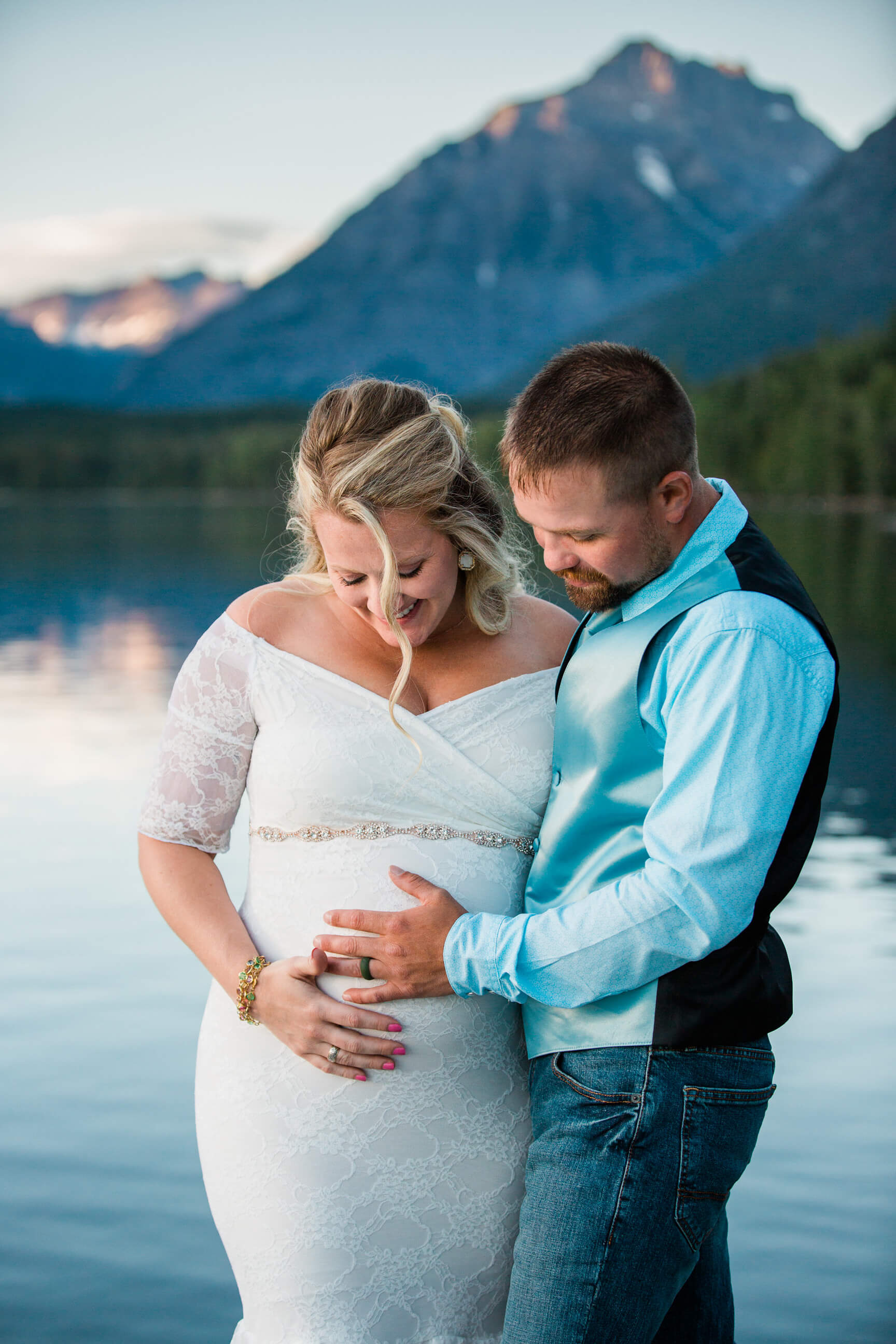 A bride and groom smile and look at the bride's pregnant belly during their elopement at Lake McDonald in Glacier National Park in Montana