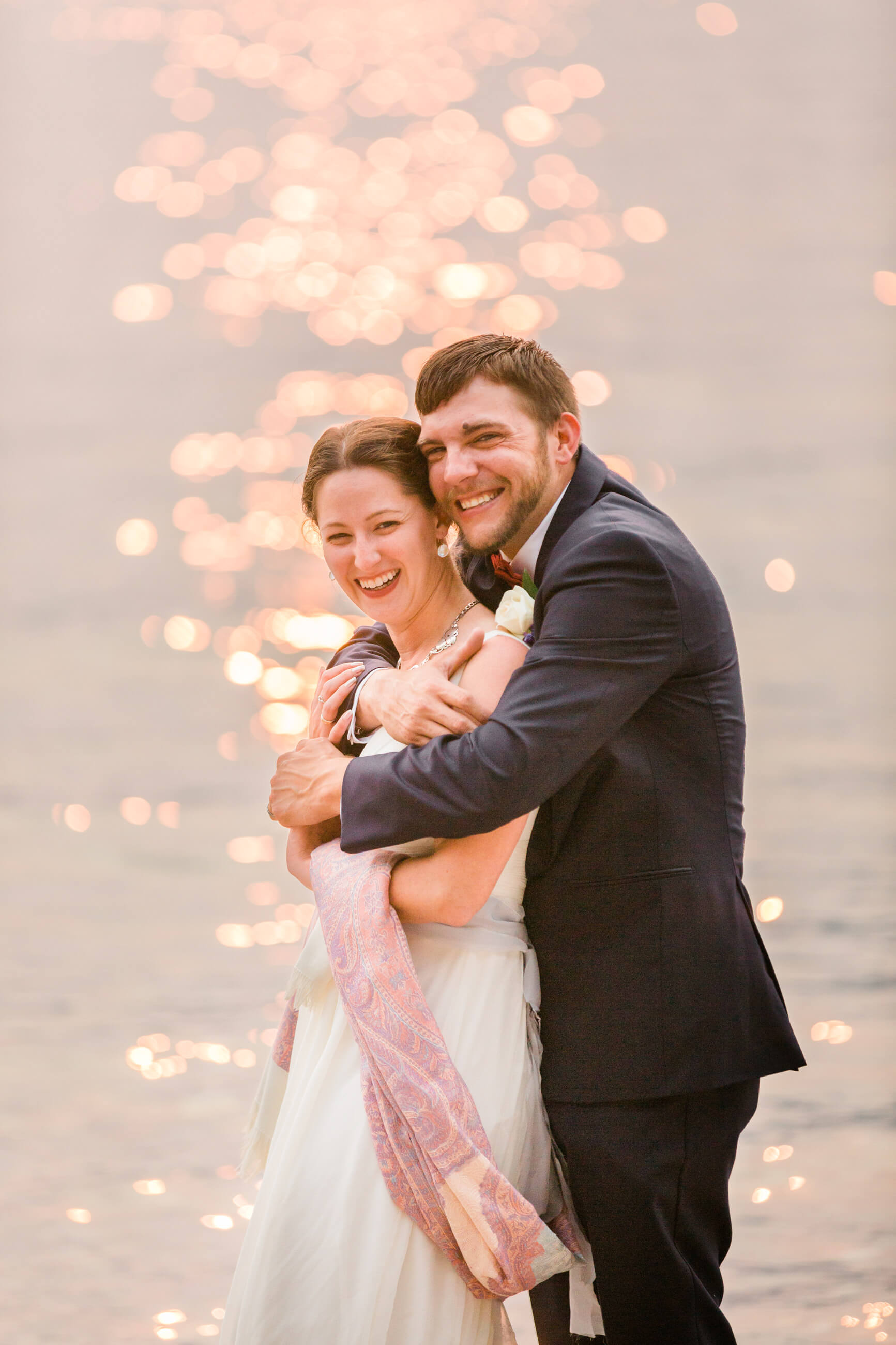 A groom hugs his bride in front of the sun shining on Lake McDonald during their Glacier National Park elopement in Montana