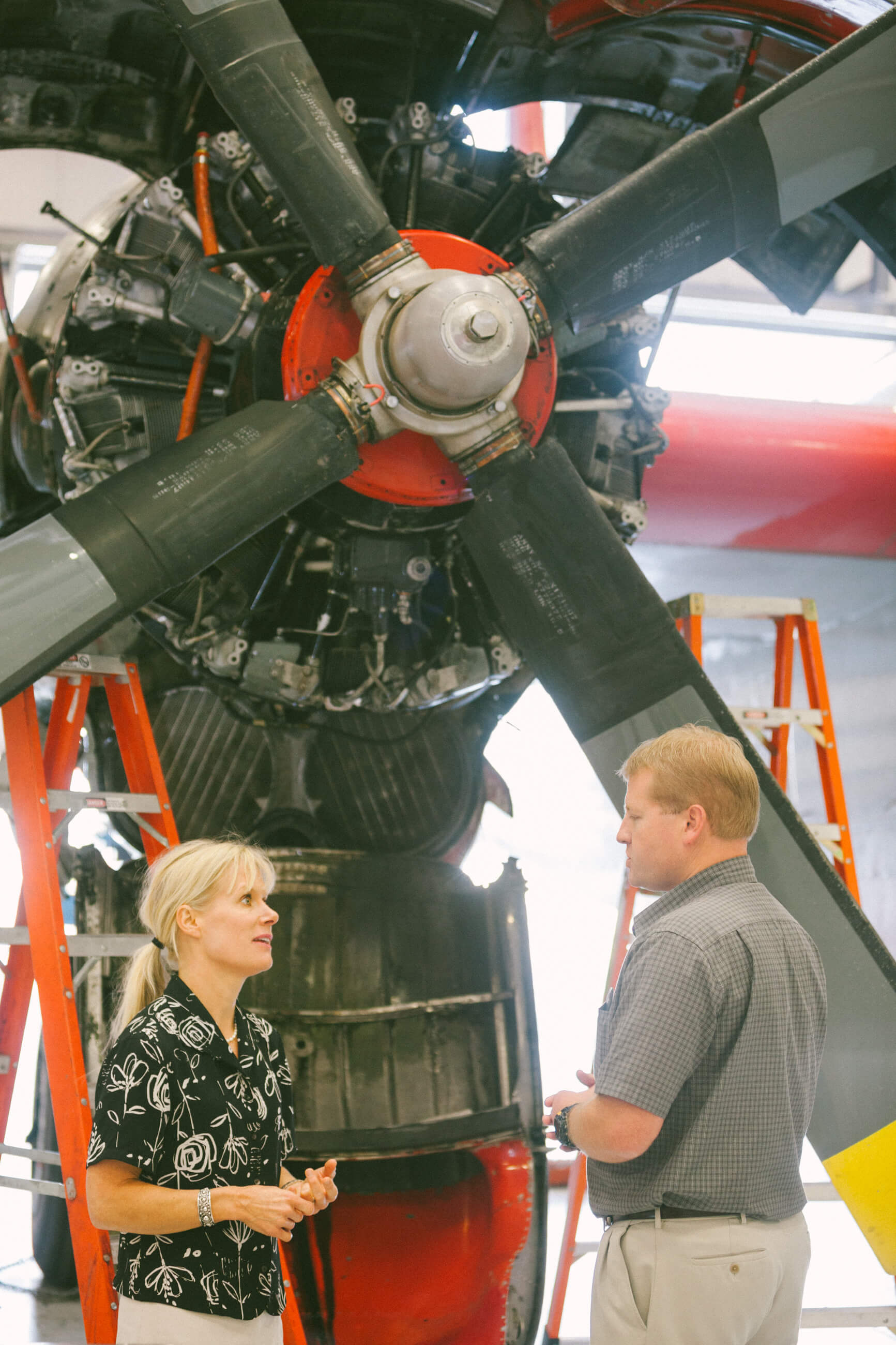 A woman speaks to a man in front of a firefighting airplane's front propeller