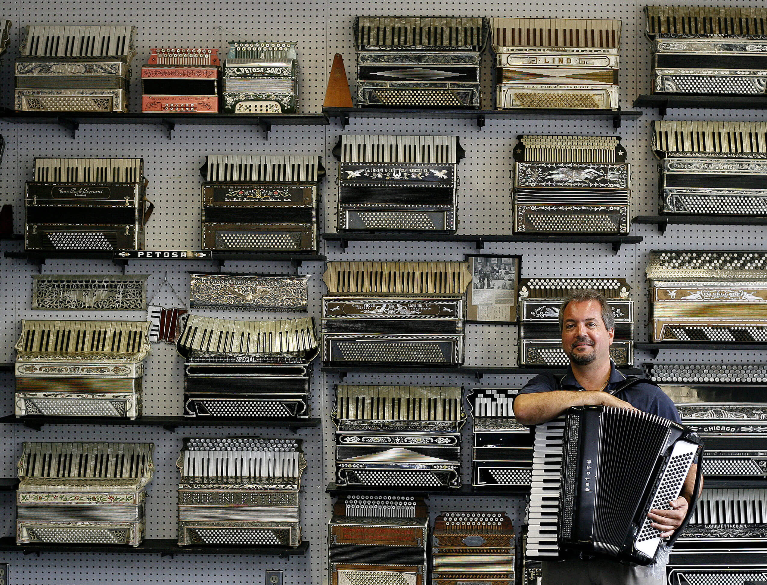 A man holds an accordion against an entire wall of accordions in Seattle Washington
