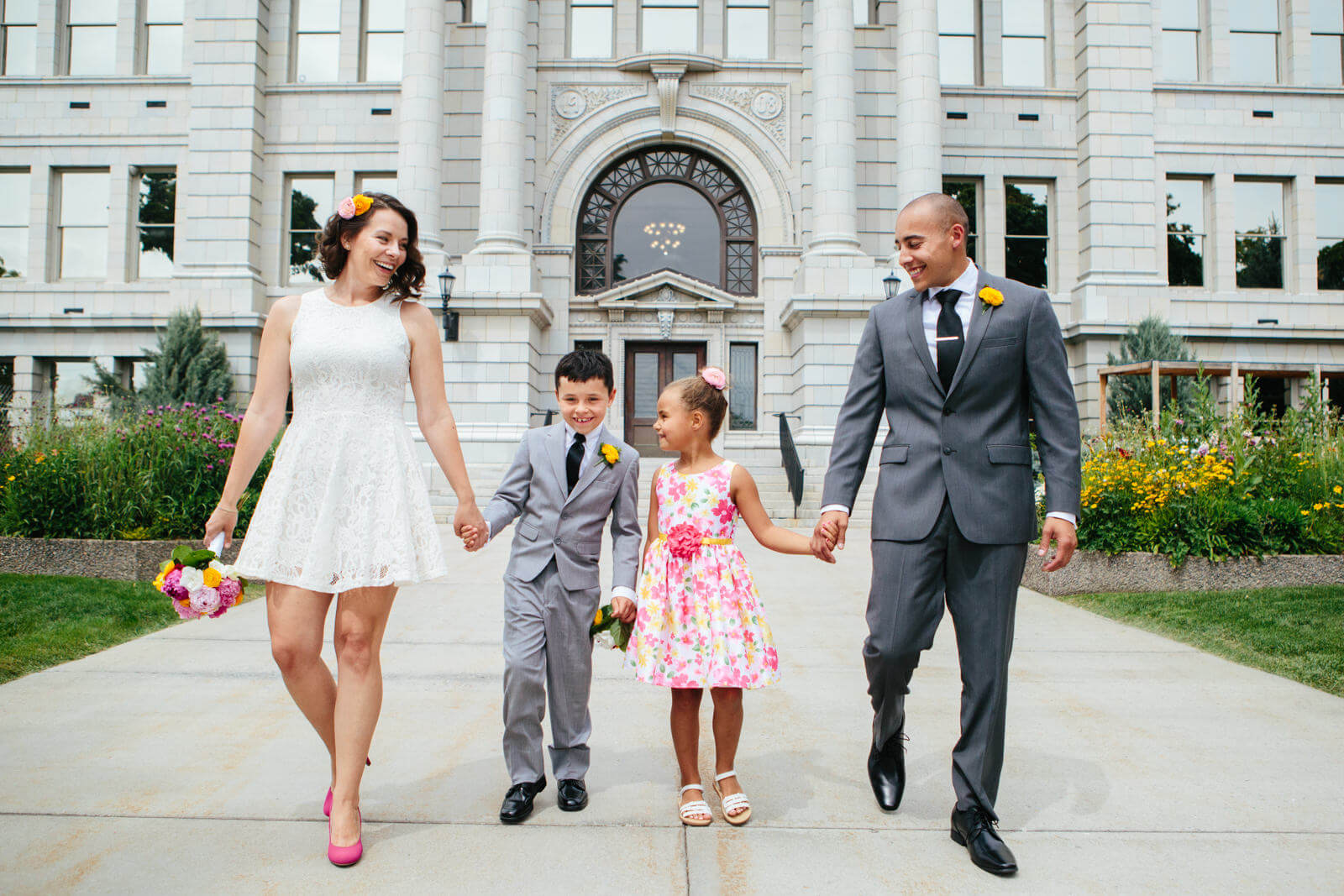 A bride and groom smile and hold the hands of their children at their Missoula County Courthouse wedding in Missoula Montana