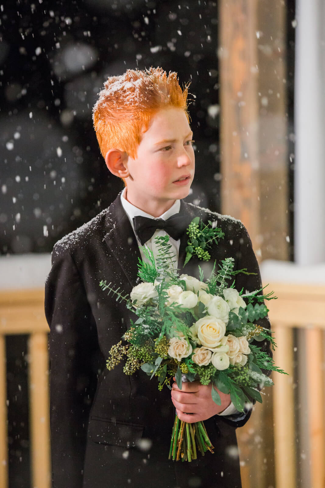 The bride's son holds her bouquet as snowflakes fly during their intimate wintertime wedding in Victor Montana