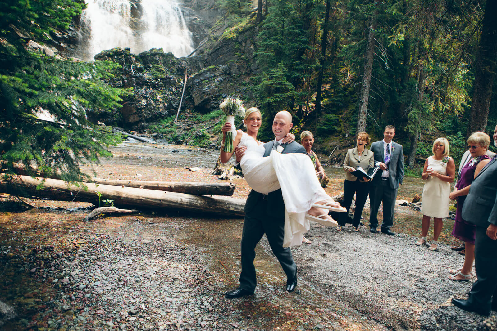A groom carries his bride over a creek during their elopement in Seeley Lake Montana