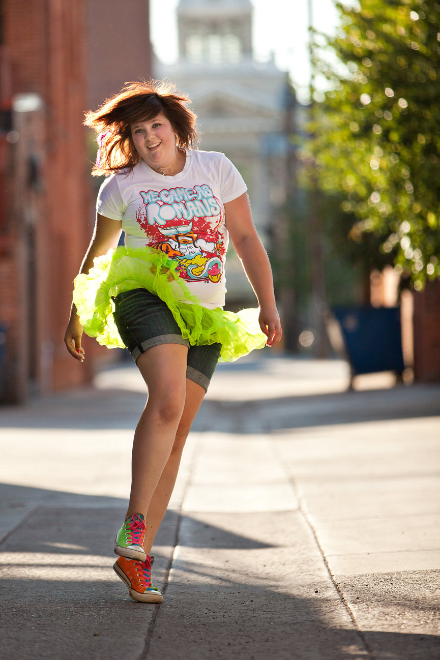 A young woman skips down an alleyway in Missoula Montana while wearing a neon green tutu and brightly colored converse sneakers