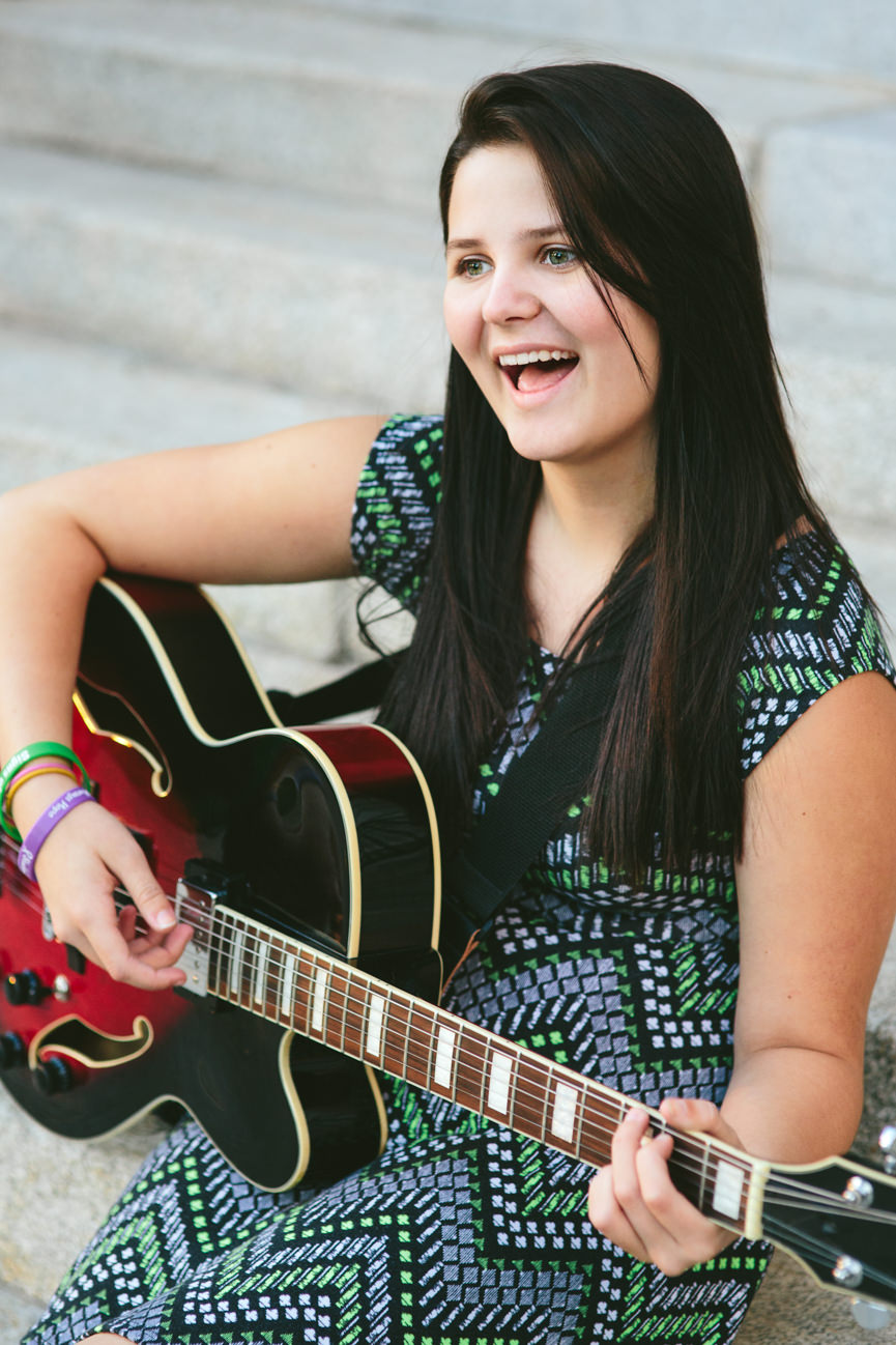 A young woman sings and plays her guitar on some steps in Missoula Montana